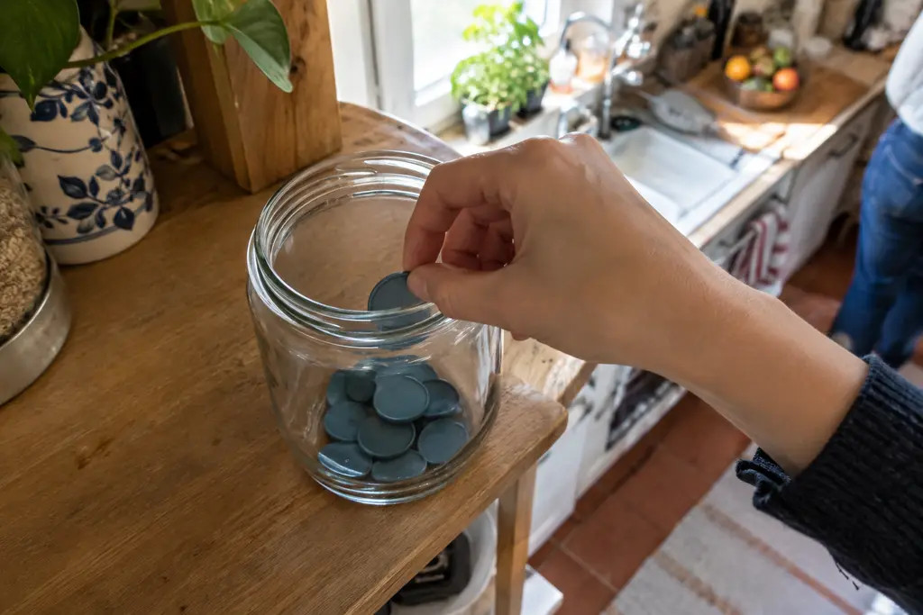Une main prend un jeton dans un bocal partiellement rempli sur une étagère.
