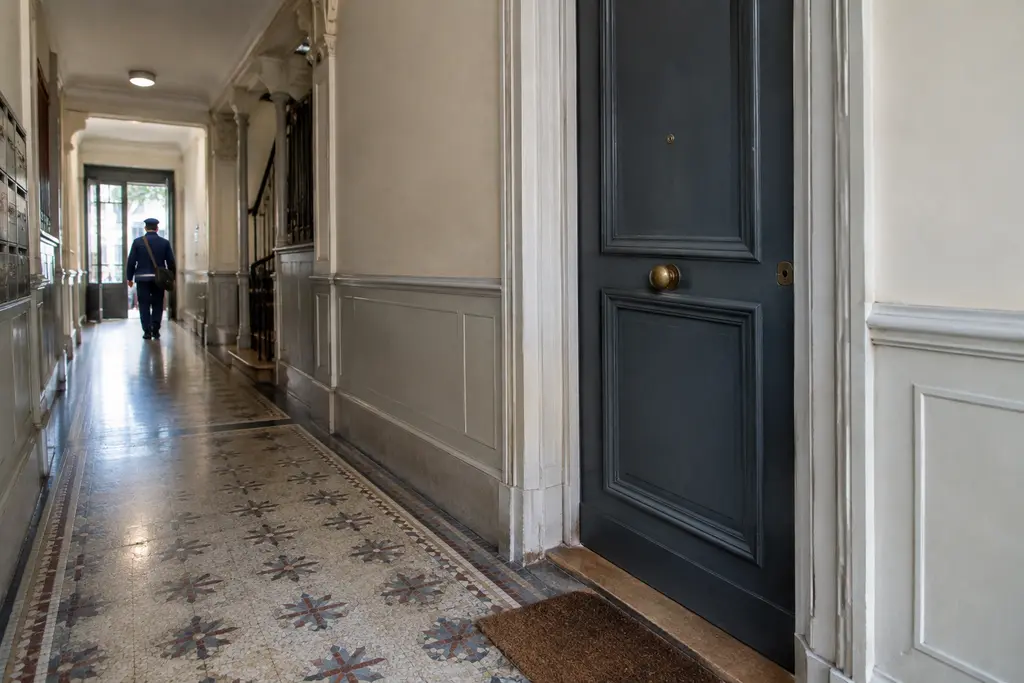 Une porte d’appartement fermée apparaît au bout d’un couloir d’immeuble ancien.
